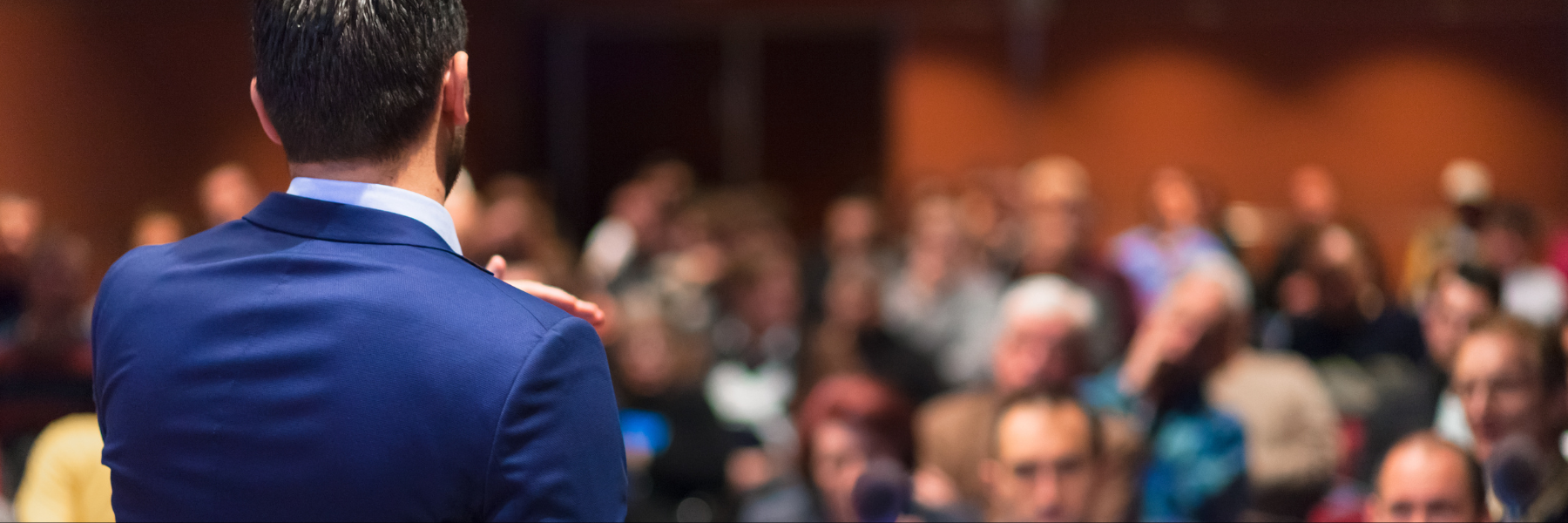 A man in a blue suit addressing a room filled with people